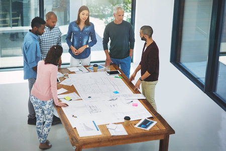 Going over the details. High angle of a group of architects looking over blueprints during a meeting...