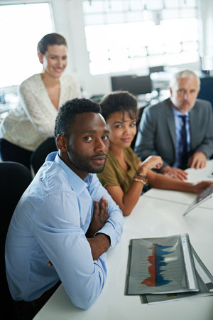 Focused on the business at hand. Portrait of a group of focused coworkers sitting at a desk in an office.の写真素材
