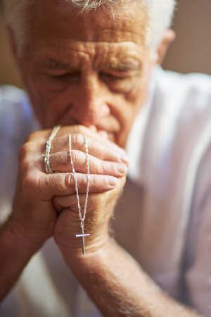 Clinging on to his belief. a senior man holding a rosary while praying for a miracle.の写真素材