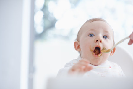 Say aaaah....Cropped image of a baby boy opening his mouth for his mother to feed him.の写真素材