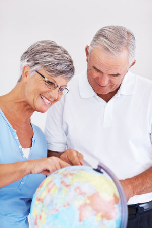 Couple searching travel destination on globe. Happy mature couple planning vacation while looking at globe.の写真素材