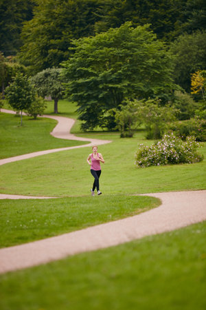 She loves to run solo. a woman jogging along a foothpath in a park.の写真素材