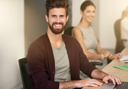 Allow me to take care of all your business needs. Portrait of a young designer sitting in an office with his colleague blurred in the background.の写真素材