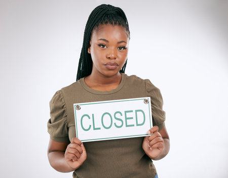 Woman, holding closed sign and studio for small business, portrait or board for bankruptcy. African entrepreneur, poster and hands with serious face, company failure or financial crisis by backgroundの写真素材