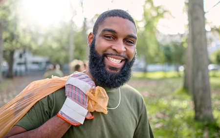 Plastic bag, park and black man cleaning for earth day, eco friendly or community service in volunteering portrait. Recycle, trash or garbage of happy ngo person in nature or forest for pollutionの写真素材