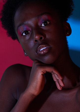 Cool, aesthetic and portrait of black woman in dark color lighting isolated on a studio background. Neon, art and face of an African girl with creativity, makeup and stylish on a creative backdropの写真素材