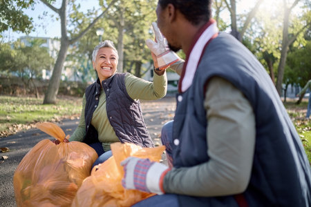 Volunteer, community service and team high five for cleaning park with bag for a clean environment. Happy man and woman helping with trash or garbage for eco friendly recycling outdoor in natureの写真素材