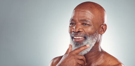 Senior black man, smile and beard in skincare for facial treatment, cosmetics or thinking on mockup. Happy elderly African American male smiling face in satisfaction against a grey studio backgroundの写真素材