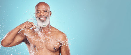 Water splash, dental and black man with toothbrush, mockup and smile on face isolated on blue background space. Teeth, toothpaste and product placement, happy senior in studio portrait cleaning mouthの写真素材