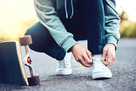 Hands, skater and man tie shoes on street to start fitness, training or workout. Sports, skateboarding and male with skateboard, tying sneaker laces on road and getting ready for exercise outdoors.の写真素材