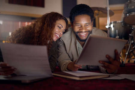 Streaming music, musician and couple with a tablet for an app, funny video and performance idea in dark. Laughing, creative and artist, song writer or black man and woman with tech for inspirationの写真素材