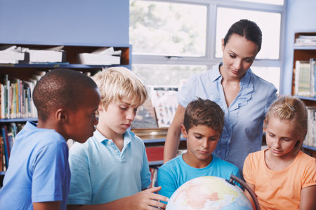 Getting to grips with geography. A pretty young geography teacher teaching her students about the world using a globe of earth.の写真素材