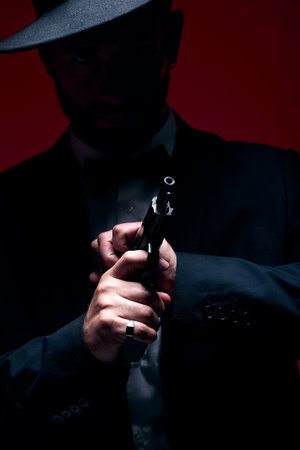 Gangster, hands or cocking gun on studio background in dark secret spy, isolated mafia leadership or crime safety. Model, assassin or hitman weapon in ready, formal style or fashion clothes aestheticの写真素材