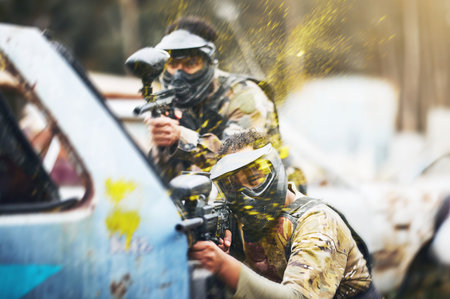 Paintball, shooting and people in action competition, game or match as a competitive team on a battleground. Aim, gun and player or teamwork of group in extreme sports with camouflage and safety maskの写真素材
