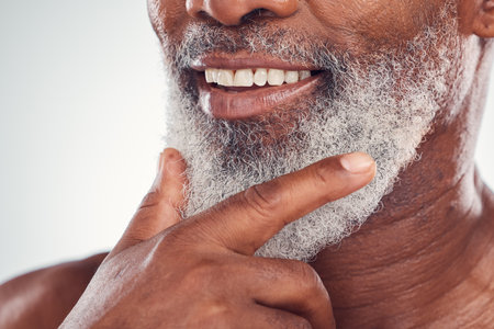 Hand, beard and smile with a senior black man grooming in studio on a gray background for beauty or skincare. Skin, hygiene and cosmetics with a mature male indoor to promote facial hair maintenanceの写真素材