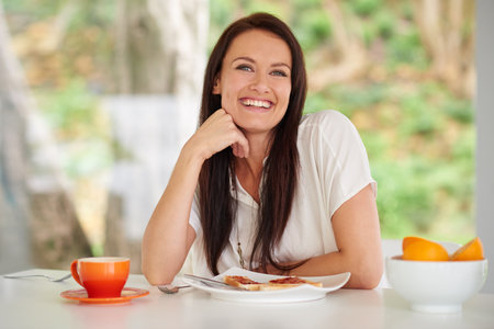 Breakfast is the most important meal of the day. a woman sitting in a kitchen eating breakfast.の写真素材