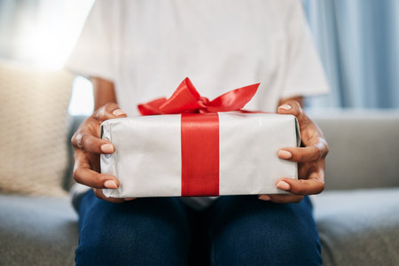 Box, gift and woman on a sofa in the living room with a giving gesture for celebration or event. Bow, wrapping paper and African female with a present for christmas, birthday or holidays in a house.の写真素材