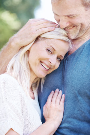 His heart still races when Im close. A beautiful woman smiling and enjoying an affectionate hug from her husband.の写真素材
