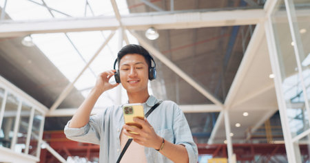 Phone, music headphones and Asian man walking in mall streaming podcast or radio. Technology, travel...