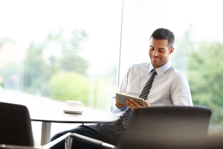 Enjoying the perfect business tool. A young businessman using a digital tablet while sitting at a table.の写真素材