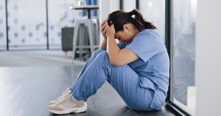 Healthcare, stress and sad nurse on floor with burnout, anxiety and headache working in emergency services. Medical care, mental health and health care worker with depression in hospital or clinicの写真素材