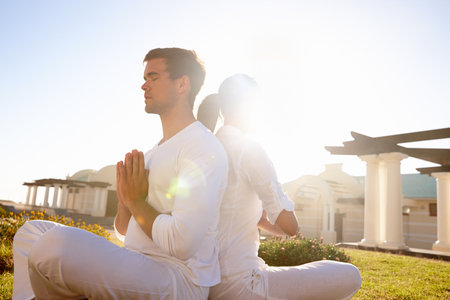 Enlightenment through the light of the sun. Full length shot of a young couple doing yoga outdoors.の写真素材