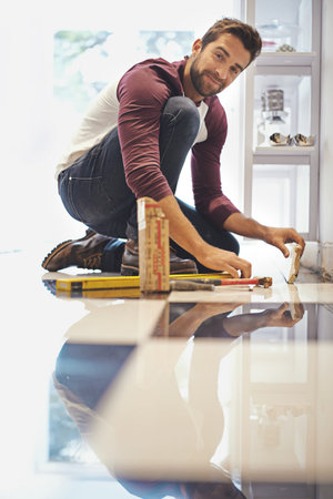 Redecorating from the floor up. Portrait of a smiling man laying floor tiles.
