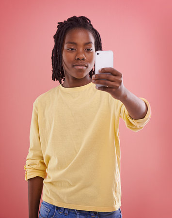 Capturing his world. Studio shot of a young boy using his smartphone against a color background.の写真素材