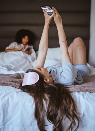 Video call, phone and relax with woman at sleepover for communication, internet and contact. Happy, online dating and smile with girl and friends in bedroom with technology, digital and social mediaの写真素材