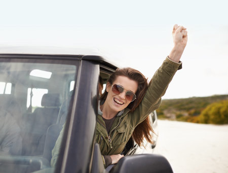 Enjoying the ride. an attractive young woman looking through the car window while on a road trip.
