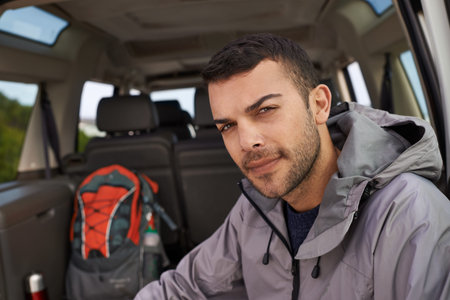 Just gotta get my gear together. Portrait of a handsome young hiker sitting at the bank of a car...