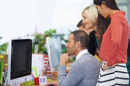 Getting the job done. three coworkers working around a single computer.