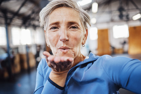 Senior woman, blowing kiss and fitness selfie at gym while happy after exercise, training or...