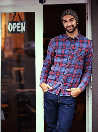 Come inside anytime you feel like it. a handsome young man posing outside a cafe with his hands...