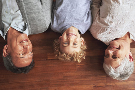 They treasure their grandson. High angle shot of a little boy lying between his grandparents on a wooden floor.の写真素材