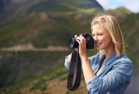 Getting a snapshot of her surroundings. A beautiful blonde holding a camera in a mountainous...