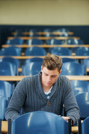 The last student in the lecture hall. A young man sitting alone in a lecture hall.の写真素材