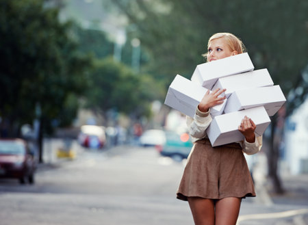 She cant get enough. A pretty young blond woman carrying a pile of clothing boxes on a downtown...