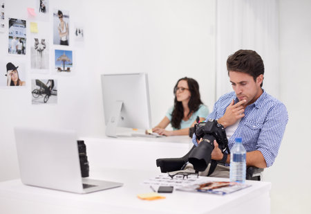 Using the tools of the trade. Two photographers sitting in their office working on layouts and...