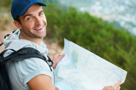 Happy with his progress. Happy young hiker smiling at the camera while holding a map.の写真素材