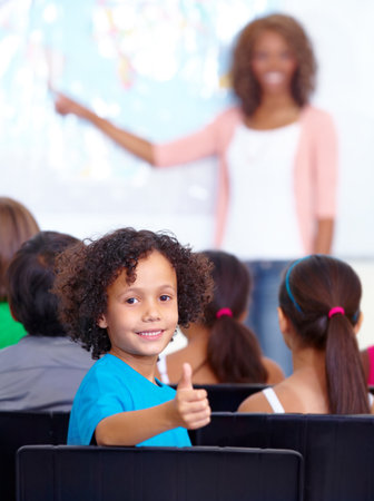 Education in action. Portrait of a young schoolboy giving you thumbs up in class.の写真素材
