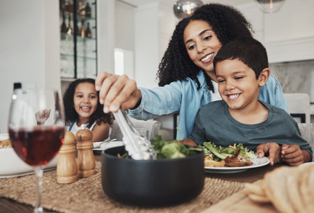 Mother, kids and eating food in home together for lunch, dinner table and healthy meal. Happy family, mom and children smile for dining in house with love, care and happiness of delicious supperの写真素材