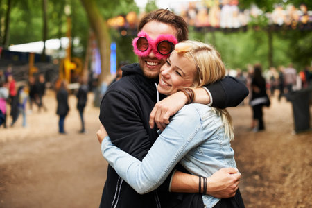 Festival loving. a young man wearing a mask hugging his girlfriend outside at a festival.