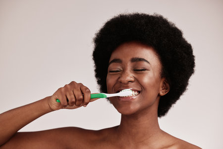 Brushing teeth, toothbrush and black woman for cleaning mouth on studio background. Face of happy person advertising dentist tips for dental care, hygiene and clean smile for healthy lifestyleの写真素材