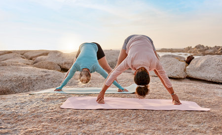 Women, yoga or stretching on beach mat for relax training, workout or exercise for healthcare wellness, muscle relief or flexibility. Friends, yogi or pilates people on rock for zen fitness at sunsetの写真素材