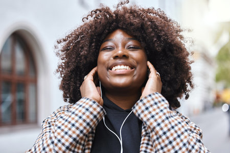 Freedom, city and black woman listening to music, radio or song in the street while walking to work. Happy, smile and African female streaming playlist, album or audio with earphones in road in town.の写真素材