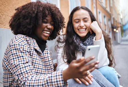 Friends, city and women with phone for social media, conversation and connection on London street. Communication, internet and happy black woman and girl on smartphone smile for selfie, app and memeの写真素材