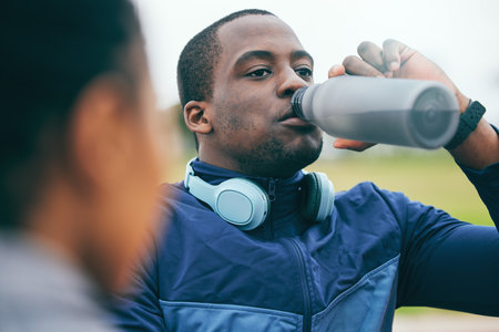 Break, fitness and black man drinking water after a race, training and sports at a stadium in Morocco. Health, relax and African athlete with a drink to hydrate after a workout, running and exerciseの写真素材