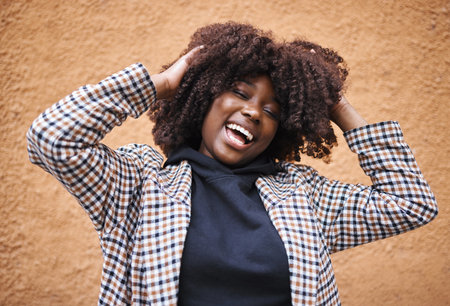 Black woman, laughing and afro for fashion, style or hair against a wall background. Portrait of happy African American female model touching stylish curls and smiling in happiness for haircareの写真素材