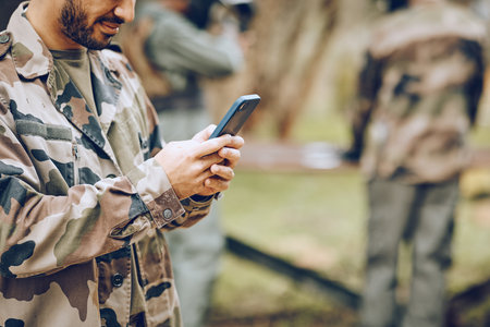 Chat, typing and man with a phone in the army for communication, social media and contact. Website, email and person reading a message on a mobile app while playing paintball on a field with friendsの写真素材